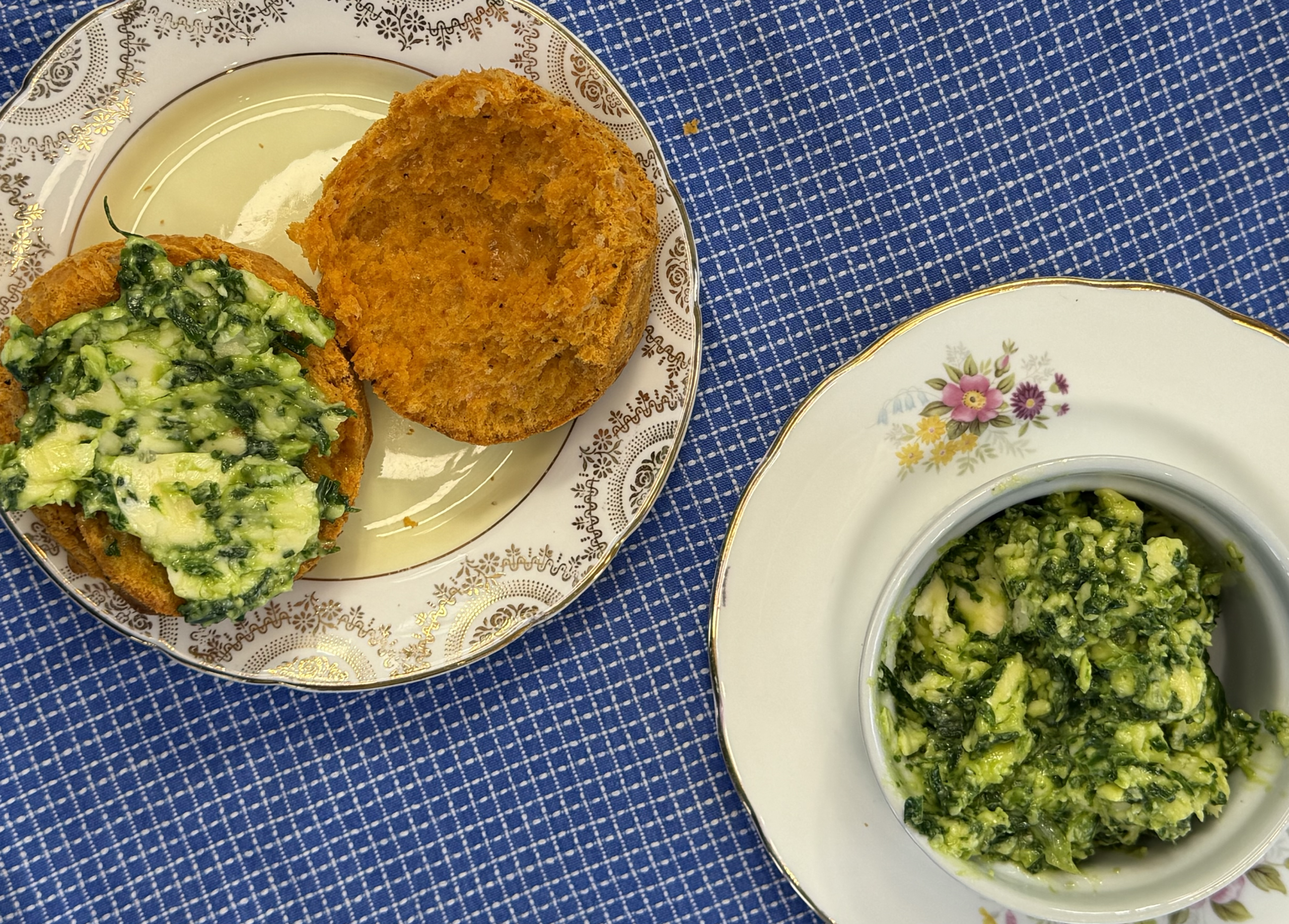 Scones on a china plate, with wild garlic butter spread over it. All dishes are layed against a blue tea towel.