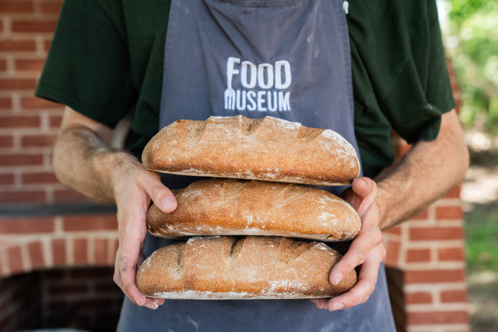 Stacked sourdough held by male hands, against Food Museum Apron, in the Bread Oven